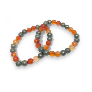 Könnte beinhalten: Zwei Armbänder aus Karneol- und Pyritperlen. Die Armbänder sind orange, gelb und grau.