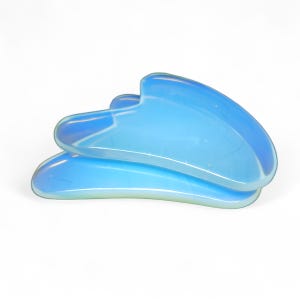 May include: Two blue jade gua sha tools, a traditional Chinese massage tool, are stacked on top of each other. The tools are made of smooth, polished jade and have a curved shape.