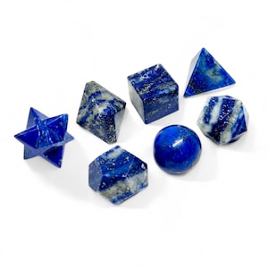 May include: Assortment of lapis lazuli gemstones in various shapes, including a sphere, cube, pyramid, and star. The deep blue stones have gold flecks and are set against a white background. These stones are ideal for crystal healing and meditation.