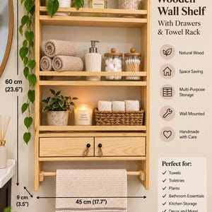 May include: A light-colored wooden wall shelf featuring three open tiers, two drawers with rope pulls, and a bottom towel rack. The unit measures 60 cm (23.6 inches) in height, 45 cm (17.7 inches) in width, and 9 cm (3.5 inches) in depth.