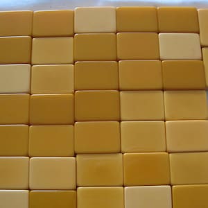 May include: A collection of rectangular mahjong tiles arranged in a grid pattern. The tiles feature a smooth, solid surface in varying shades of yellow, ranging from a pale cream color to a deeper, saturated golden mustard yellow tone.