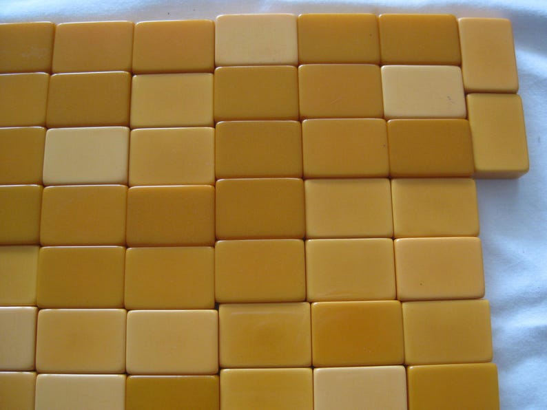 May include: A collection of rectangular mahjong tiles arranged in a grid pattern. The tiles feature a smooth, solid surface in varying shades of yellow, ranging from a pale cream color to a deeper, saturated golden mustard yellow tone.