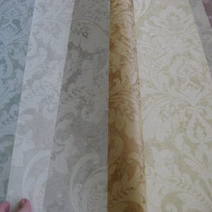 May include: A selection of wallpaper samples featuring various colors and patterns. The designs include floral and scroll motifs in shades of green, gray, beige, and brown. The samples are arranged side by side, showcasing the different color variations.