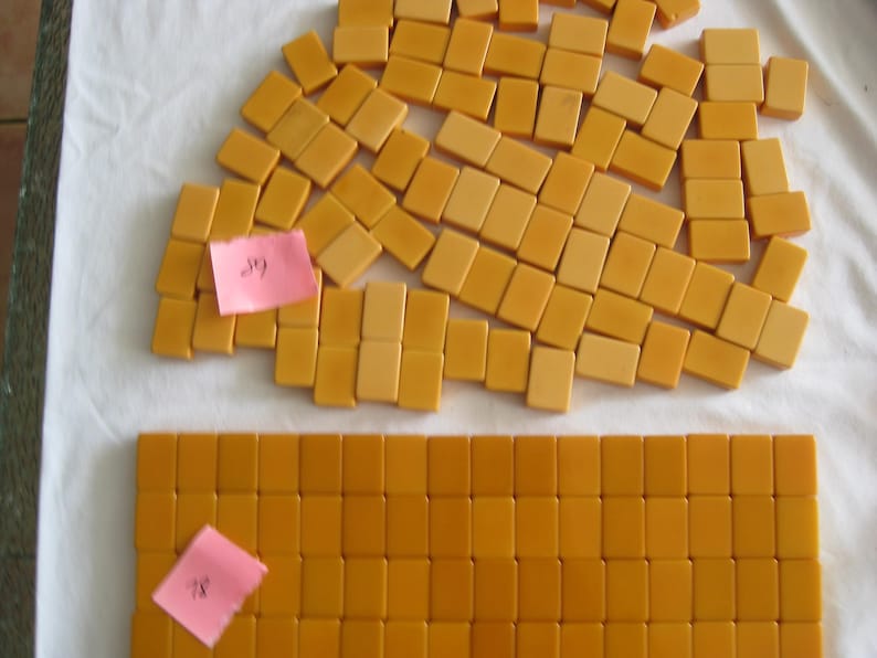 May include: A collection of rectangular, mustard-yellow mahjong tiles arranged in a large, loose cluster and a neat, organized rectangular grid. Two small, pink adhesive notes with handwritten numbers are attached to the tile groups.