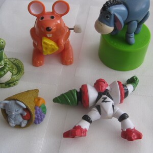 May include: A collection of five colorful wind-up toys. The toys include a green alligator, a red and orange mouse, a white and green robot, a brown and white bunny, and a blue Eeyore character from Winnie the Pooh.