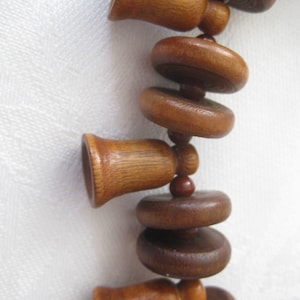 May include: A wooden necklace with brown and dark brown beads. The beads are in the shape of bells and circles. The necklace is strung together with small brown beads.