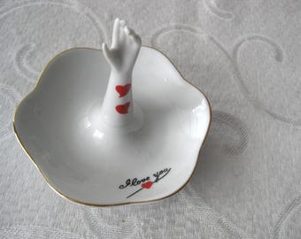 White ceramic ring dish w red hearts on a raised hand.