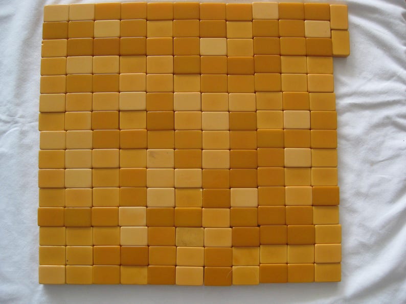 May include: A collection of rectangular tiles arranged in a grid pattern, featuring a mix of light yellow and deep mustard yellow colors. The tiles are laid out in a square formation with a few extra tiles extending from the top right corner.