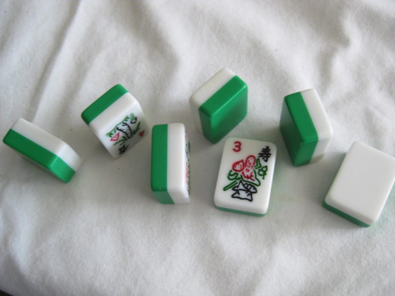 K&ouml;nnte beinhalten: Eine Ansammlung wei&szlig;er und gr&uuml;ner Mahjong-Steine. Die Steine haben gr&uuml;ne Kanten und sind oben und an den Seiten wei&szlig;. Einige Steine zeigen Illustrationen und die Zahl "3". Die Steine liegen auf einer wei&szlig;en Oberfl&auml;che.