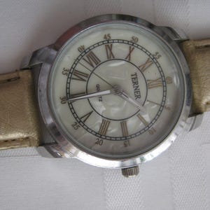 Bijoux Terner stainless steel wrist watch, mother of pearl face, Roman numbers, antique gold tone band.