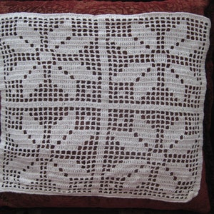 May include: White crocheted doily with a floral pattern. The doily is laid on a red fabric surface.