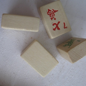 May include: A set of white wooden mahjong tiles with red and green markings. The tiles are arranged on a white surface. One tile has the number 1 and a red symbol, another tile has the number 1 and a green symbol, and the other tiles are blank.