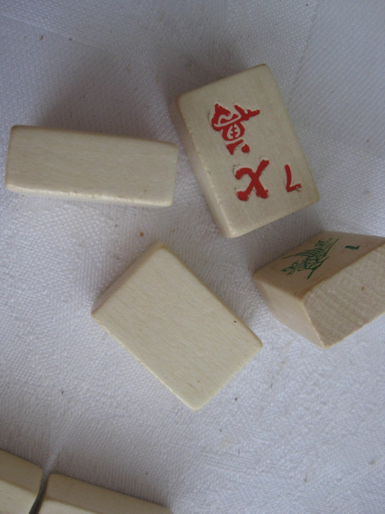 May include: A set of white wooden mahjong tiles with red and green markings. The tiles are arranged on a white surface. One tile has the number 1 and a red symbol, another tile has the number 1 and a green symbol, and the other tiles are blank.