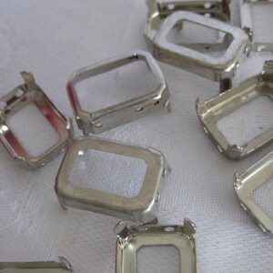 May include: A collection of silver-toned metal rectangular settings for jewellery making. Each piece features a hollow centre with four small prongs extending from the corners, designed to hold a stone or cabochon securely in place.
