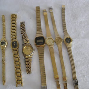 May include: A collection of gold-toned wristwatches with various designs. The watches feature different styles of watch faces, including digital displays and analog faces with black or gold hands. The bands vary in style, from linked bracelets to thin, flexible straps.