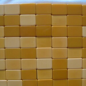 May include: A collection of rectangular mahjong tiles arranged in a grid pattern. The tiles feature a smooth, solid surface in alternating shades of cream and mustard yellow, creating a uniform, block-like appearance across the entire display.