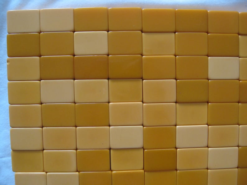 May include: A collection of rectangular mahjong tiles arranged in a grid pattern. The tiles feature a smooth, solid surface in alternating shades of cream and mustard yellow, creating a uniform, block-like appearance across the entire display.