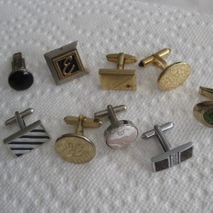 May include: A collection of ten cufflinks in various styles and colors. Some cufflinks are silver, some are gold, and some have a patterned design.