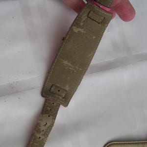 K&ouml;nnte beinhalten: Ein braunes Lederarmband mit einem rosafarbenen Lederband und einer silbernen Schlie&szlig;e. Das Armband hat mehrere L&ouml;cher zum Einstellen der Gr&ouml;&szlig;e.