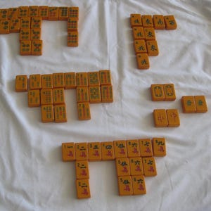 May include: A collection of orange Mahjong tiles arranged on a white surface. The tiles display various symbols, numbers, and Chinese characters. The game pieces are organized in several distinct groups, showcasing the game's components.