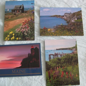 May include: Four postcards featuring scenic views. One shows a house near the ocean with colorful flowers. Another depicts a coastal scene with a house and blue water. A third postcard displays a lighthouse at sunset. The last shows a pier and boats.