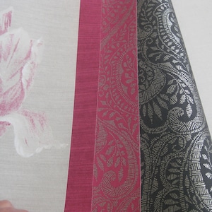 May include: Three samples of patterned wrapping paper. The first is a solid red, the second is red with a silver paisley pattern, and the third is black with a silver paisley pattern.