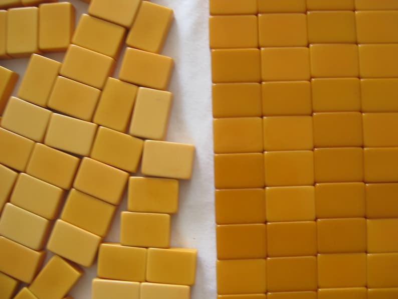 May include: A collection of rectangular mustard-yellow mahjong tiles. On the left, the tiles are scattered in an irregular, overlapping arrangement. On the right, the tiles are organized into a neat, uniform grid of rows and columns.