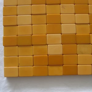 May include: A grid of rectangular tiles arranged in a repeating pattern of alternating light cream and golden yellow colors. The tiles are smooth and uniform in shape, creating a flat, structured surface with a consistent, clean geometric layout.