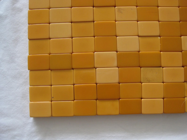 May include: A grid of rectangular tiles arranged in a repeating pattern of alternating light cream and golden yellow colors. The tiles are smooth and uniform in shape, creating a flat, structured surface with a consistent, clean geometric layout.