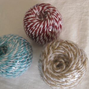 May include: Three balls of twine in different colors: red and white, blue and white, and tan and white. The twine is tightly wound into spherical shapes and wrapped in clear plastic.