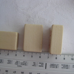 May include: Three rectangular wooden blocks, each with a different size. The blocks are light brown in color and are arranged in a row from smallest to largest.