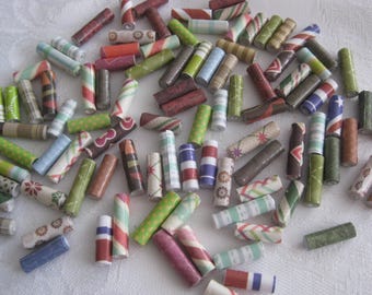 May include: A collection of colorful, patterned paper beads. The beads are made from rolled up paper and have a variety of designs, including stripes, polka dots, and floral patterns.