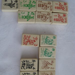 May include: A set of 12 mahjong tiles with various numbers, symbols, and Chinese characters. The tiles are white with black, red, and green markings. The tiles are arranged in three rows of four.
