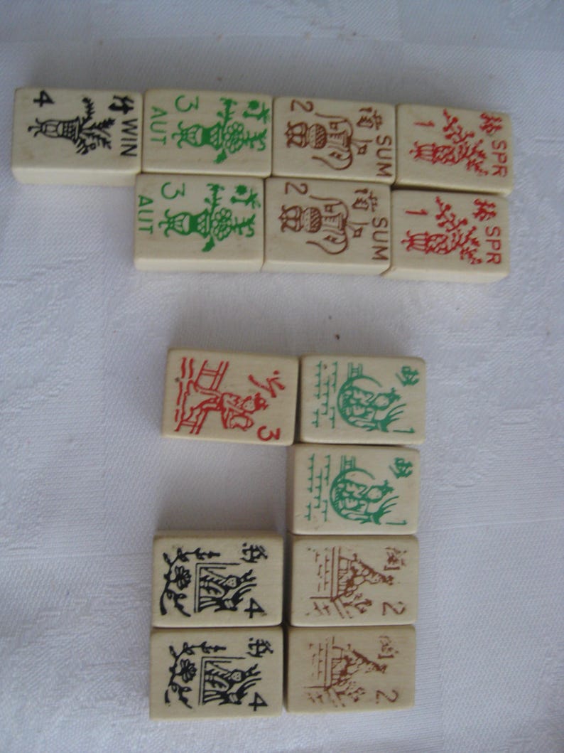 May include: A set of 12 mahjong tiles with various numbers, symbols, and Chinese characters. The tiles are white with black, red, and green markings. The tiles are arranged in three rows of four.