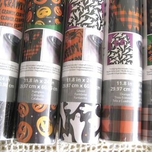 May include: Five rolls of Halloween-themed adhesive vinyl sheets, each measuring 11.8 inches by 24 inches. The patterns include spiderwebs, orange pumpkins, white ghosts, orange and black plaid, and a black and white plaid with pumpkin icons.