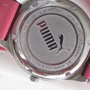 K&ouml;nnte beinhalten: Eine silberfarbene Uhr mit einem rosafarbenen Lederarmband. Das Zifferblatt der Uhr ist von einer silbernen L&uuml;nette mit dem Text "100 Meter wasserdicht - Japanisches Quarzwerk - Ganz aus Edelstahl" und dem Puma-Logo umgeben.