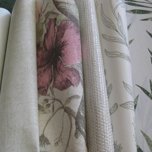 May include: Rolled wallpaper samples showcasing various floral and textured designs. The samples include a white, light gray, and a floral pattern with a large pink flower. Other patterns feature green leaves and a woven texture.