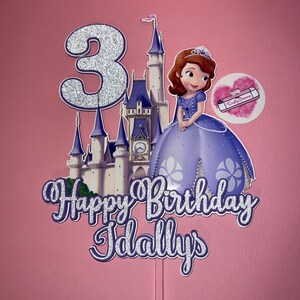 May include: A silver glitter cake topper with a princess castle, a princess character, and the words "Happy Birthday Idallys" and the number "3".