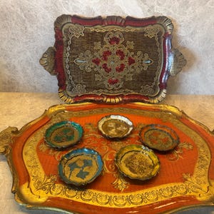 Op de afbeelding: Twee decoratieve trays met sierlijke ontwerpen. De grotere tray is oranje met gouden randen en bevat vijf kleine, kleurrijke schaaltjes. De kleinere tray is rood en goud met een centraal ontwerp.