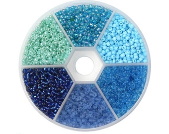 May include: A round plastic container with six compartments filled with different shades of blue and green seed beads.  The container is divided into six sections, each containing a different color of beads.  The beads are small and round, and they are perfect for jewelry making.