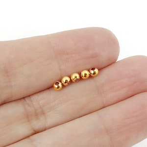 May include: A close-up of a hand holding a line of six gold-coloured metal beads.