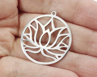 May include: Silver-toned metal charm featuring a cutout design of a lotus flower. The charm is round and has a hole at the top for attaching to a necklace or bracelet.