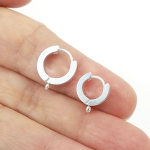 May include: A pair of silver hoop earrings with a small ball charm hanging from each hoop.