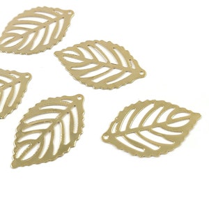 May include: Five gold-coloured, openwork leaf charms. Each charm has a detailed vein pattern and a small hole at the top for stringing. The leaves are scattered against a white background, ideal for jewellery making or craft projects.