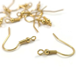 Peut inclure: Gros plan sur des crochets de boucles d'oreilles dorés avec une petite boule au sommet de chaque crochet. Les crochets sont en métal et ont une fermeture à ressort.
