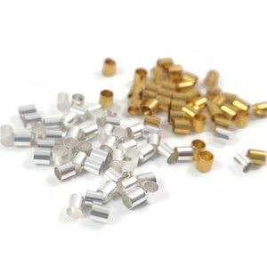 May include: A pile of silver and gold metal crimp beads. The beads are small and cylindrical.