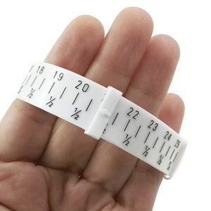 May include: White plastic ring sizer with black markings for sizes 18 to 25. The sizer is shown being used on a person's finger.