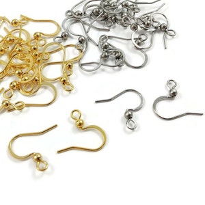 May include: A close-up of a pile of gold and silver earring hooks. The hooks are made of metal and have a small ball at the top. There are about 20 hooks in total.