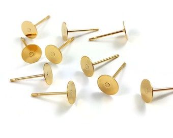 May include: A group of ten gold-colored earring posts with flat round backs. The posts are scattered on a white surface.