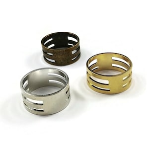 May include: Three metal rings with three horizontal lines cut out. The rings are silver, gold, and bronze.